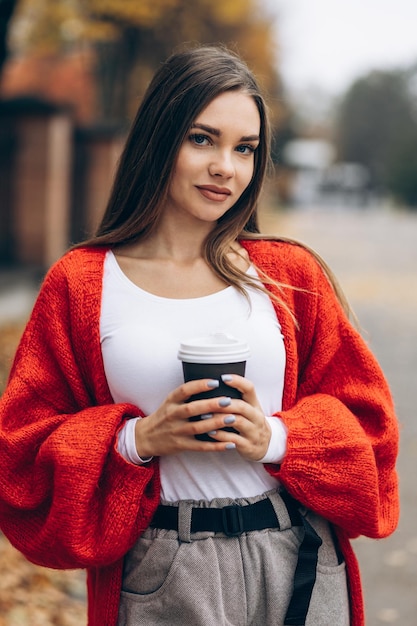 커피를 마시고 가을 거리를 걷는 젊은 여자