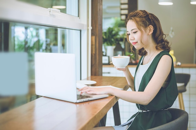 テーブルの上でラップトップを使用しながらコーヒーを飲んでいる若い女性