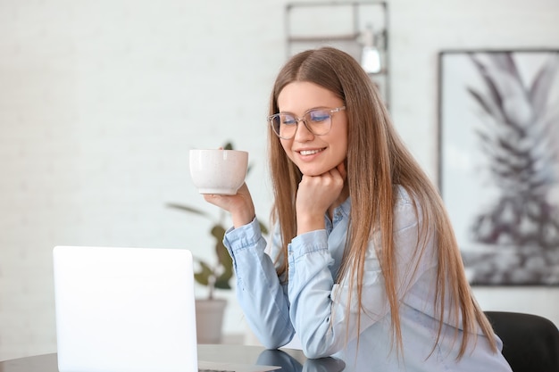 カフェでノートパソコンで作業しながらコーヒーを飲む若い女性