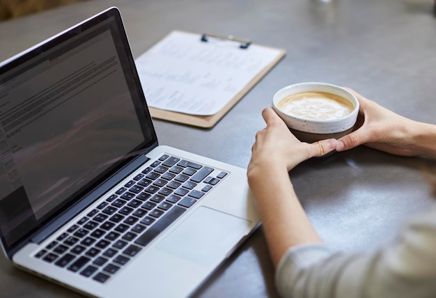 カフェでノートパソコンで作業しながらコーヒーを飲む若い女性