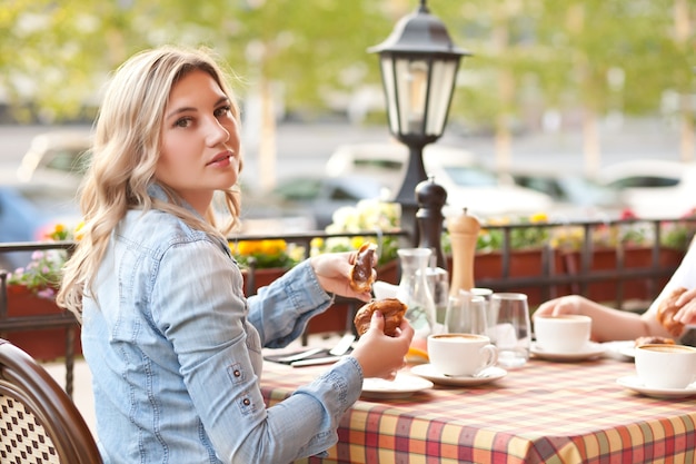 友達とカフェ テラスでクロワッサンとコーヒーを飲む若い女性