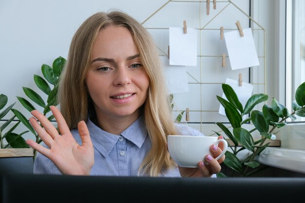 Фото Молодая женщина пьет кофе, работает на компьютере дома, рассчитывает ежемесячные расходы по ипотеке.