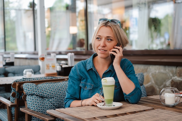 Young woman drinking enjoying matcha green tea latte in summer morning in cafe.