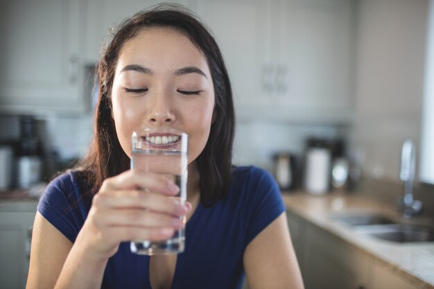 キッチンで水のガラスを飲む若い女性