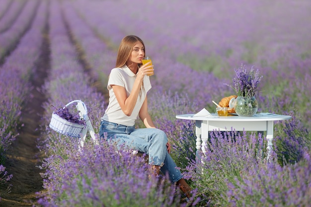 Giovane donna che beve succo in un campo di lavanda