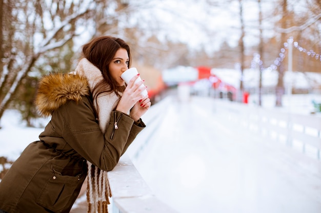 Фото Молодая женщина пьет чай или кофе над зимним природным пространством на открытом воздухе