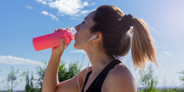 ヘッドフォンで音楽を聴いて走った後、水を飲む若い女性健康的なライフスタイル