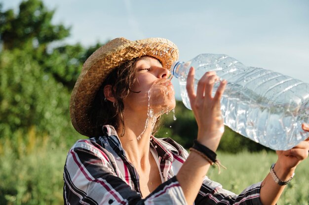 Foto giovane donna che beve acqua contro gli alberi e il cielo