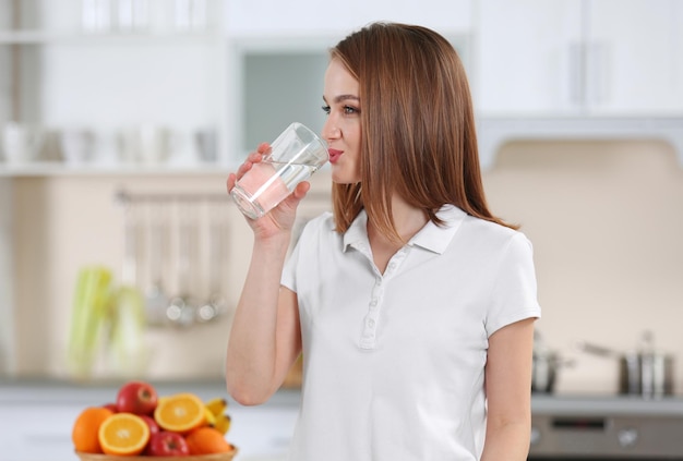 Young woman drinking water from glass in the kitchen