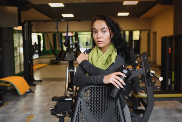 Young woman drinking water and taking a break after workout in gym,