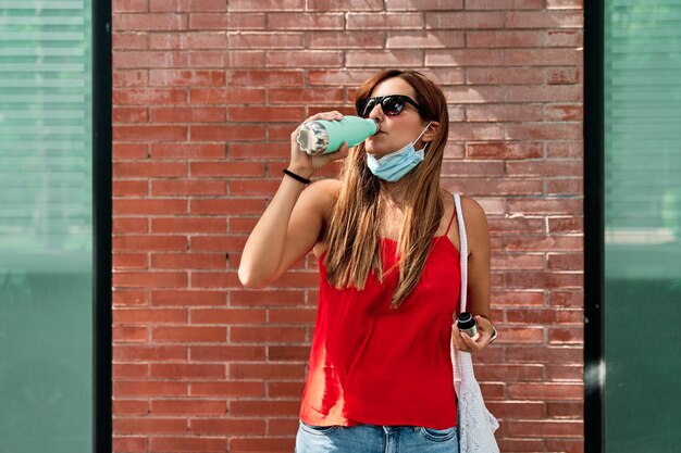 Young woman drinking water while wearing mask