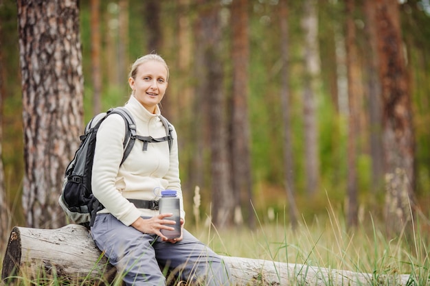 Young woman drinking water with backpack at forest valley