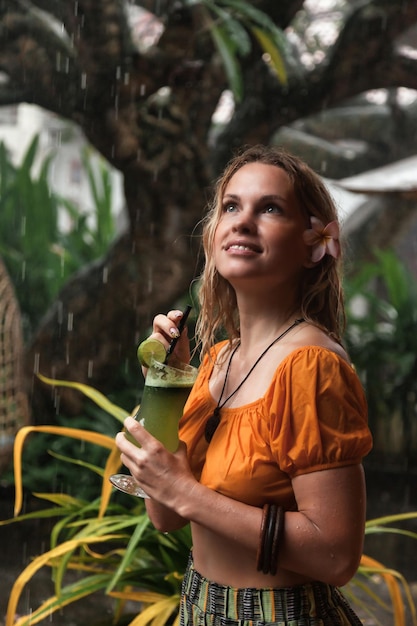 Young woman drinks cocktail in tropical rain