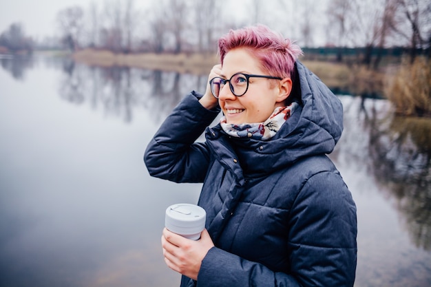 Young woman drinks coffee cup on lake shore