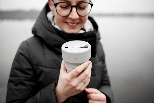 若い女性は湖岸でコーヒーカップを飲みます