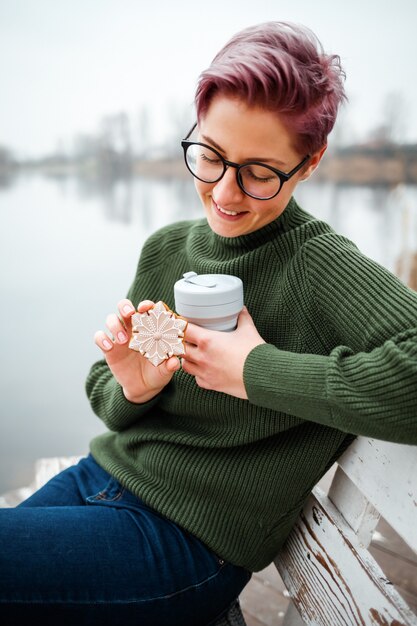 若い女性は湖岸でコーヒーカップを飲みます