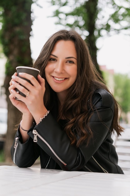 若い女性が外で紙コップからコーヒーを飲む