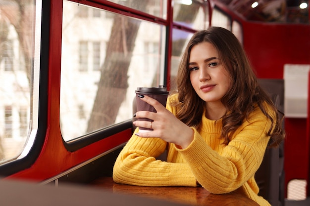 La giovane donna beve il caffè dal bicchiere di carta sul trasporto pubblico