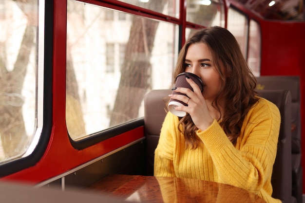 Young woman drinks coffee from paper glass