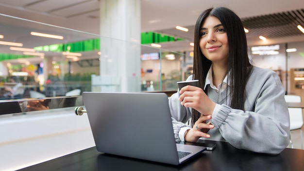 A young woman drinks coffee while working at a laptop