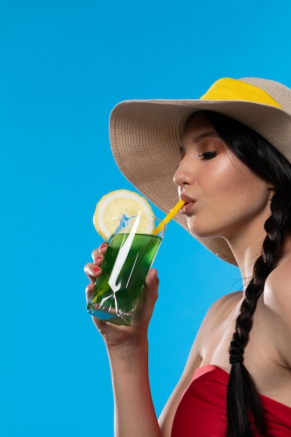 A young woman drinks a drink on a hot summer day and has a hat on her head