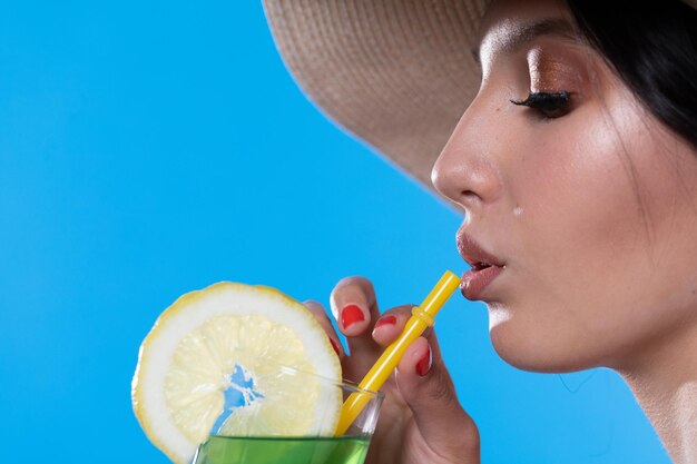 A young woman drinks a drink on a hot summer day and has a hat on her head