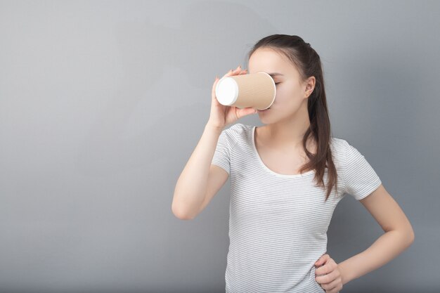 Young woman drinks hot drink on gray background