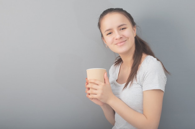 Young woman drinks hot drink on gray