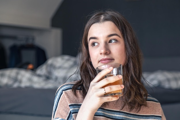 若い女性が部屋に座ってジュースを飲む