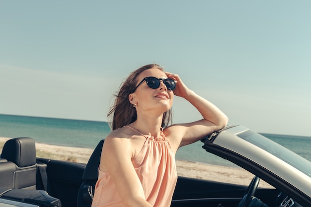 若い女性はビーチで車を運転します