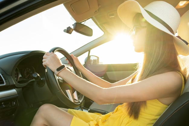 Фото Молодая женщина-водитель в летнем желтом платье и соломенной шляпе за рулем автомобиля
