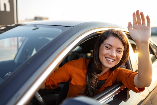 Photo young woman driving car and waving close up portrait of young business woman sitting in the car and laughing while waving