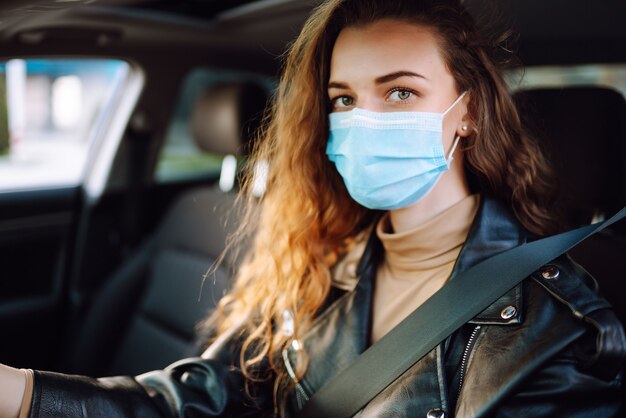 Young woman driving a car wearing on a medical mask during an epidemic. Transport isolation. Covid-2019.