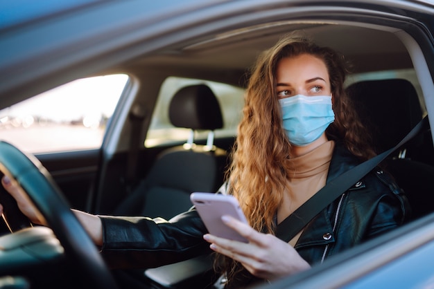 Young woman driving a car wearing on a medical mask during an epidemic. Transport isolation. Covid-2019.