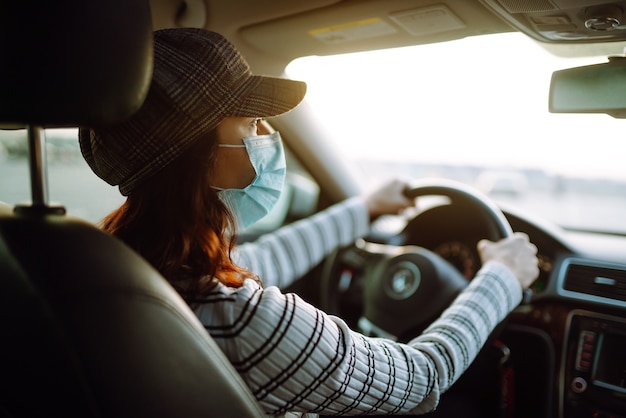Giovane donna alla guida di un'auto con maschera protettiva sul viso. isolamento del trasporto.