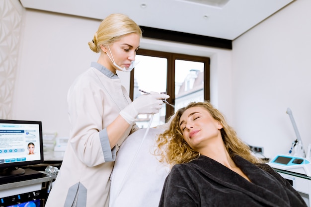 Photo young woman during the professional hydration procedure on the face in the cosmetological office. professional woman cosmetologyst holds splutter for hydration procedure spraying water