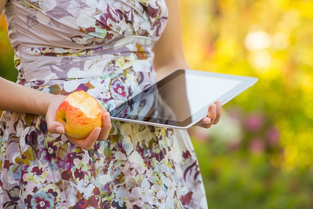 Young woman eat apple and play on tablet pc in park