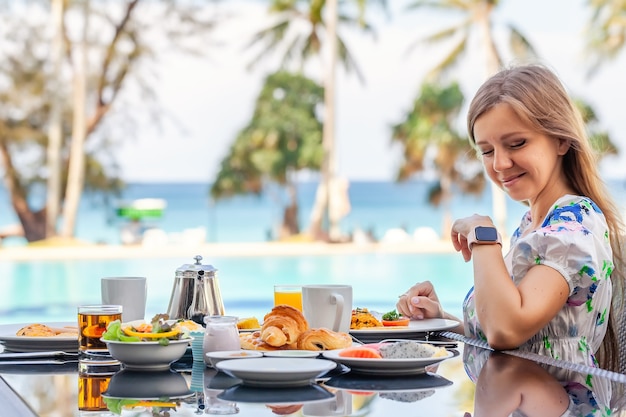 젊은 여성은 리조트 레스토랑 수영장 청록색 바다 배경에서 아침 식사를 먹습니다.
