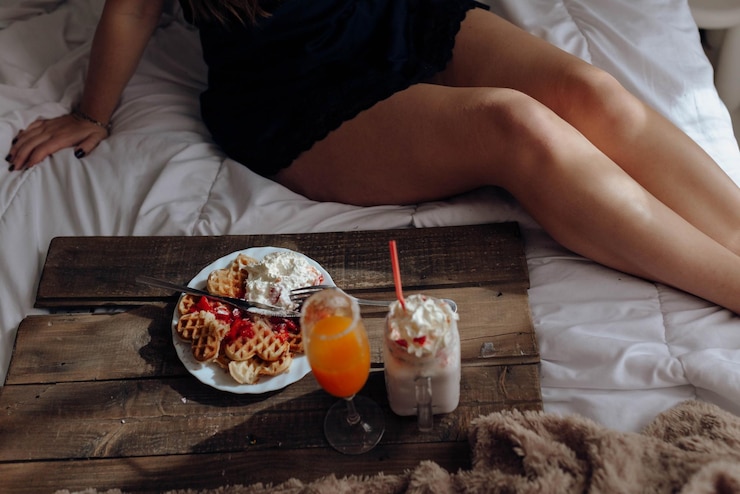 Photo young woman eating appetizing waffles and tasty drinks on tray on bed