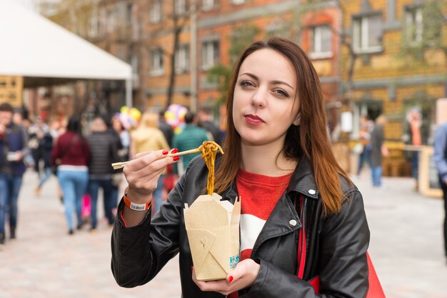 Photo young woman eating asian take out at busy festival