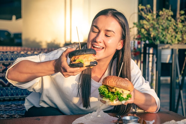 A young woman eating burger in street cafe close up