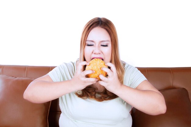 Photo young woman eating burger while sitting on sofa