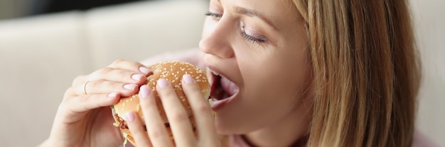 Young woman eating delicious appetizing hamburger at home