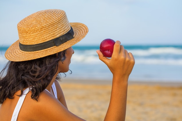 Giovane donna che mangia frutta sulla spiaggia