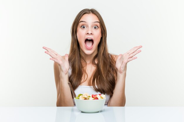 Young woman eating fruit bowl celebrating a victory or success