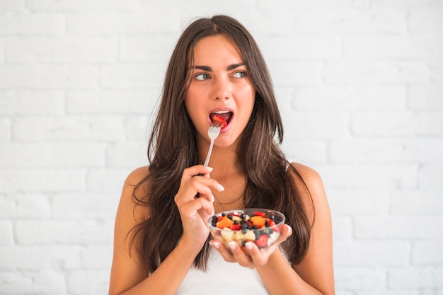 Молодая женщина, едят фруктовый салат с вилкой