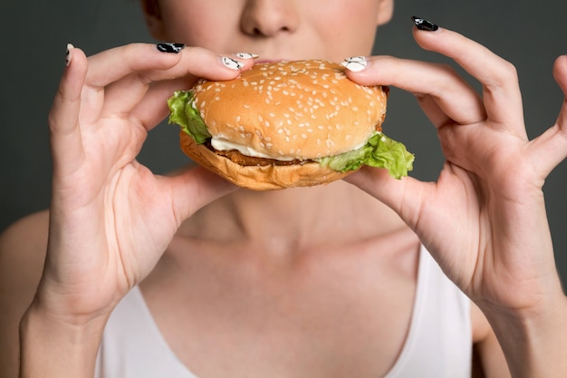 Young woman eating hamburger on gray background. 