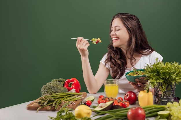 背景に緑の壁と美しいインテリアに座って健康的な食べ物を食べる若い女性