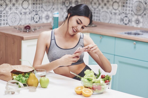 Young woman eating healthy salad with cherry tomatoes in the kitchen after a fitness session