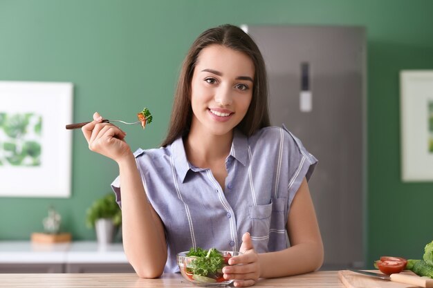 Молодая женщина ест здоровый салат с овощами на кухне